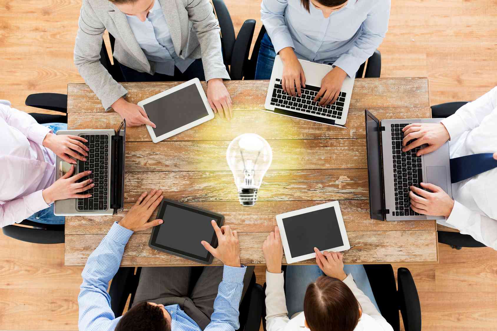Équipe collaborant autour d'ordinateurs portables et de tablettes avec une ampoule d'idée au centre